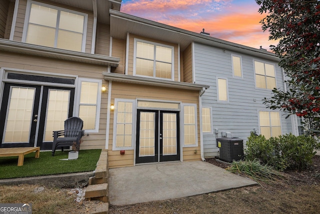 back house at dusk with french doors, central AC unit, and a patio area