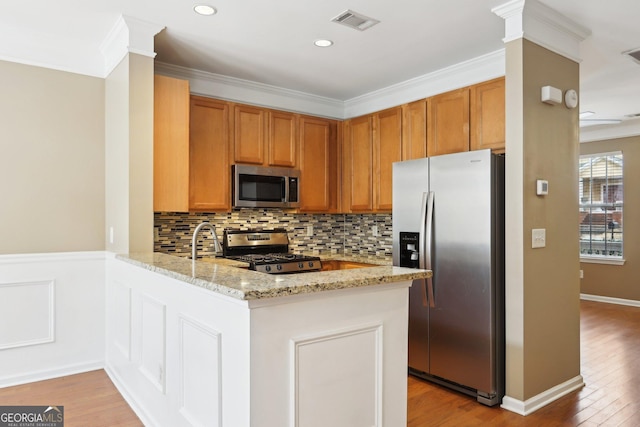 kitchen with light stone counters, ornamental molding, kitchen peninsula, stainless steel appliances, and light hardwood / wood-style floors