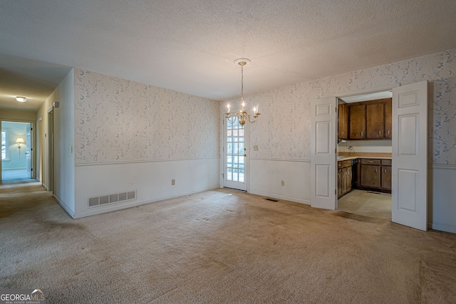 unfurnished dining area with light carpet, a notable chandelier, and a textured ceiling