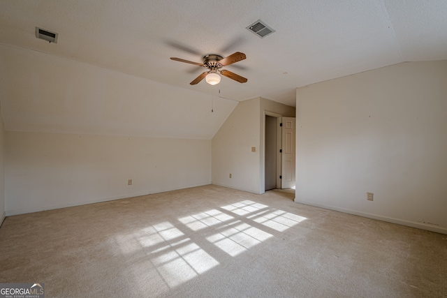 additional living space with ceiling fan, vaulted ceiling, light carpet, and a textured ceiling