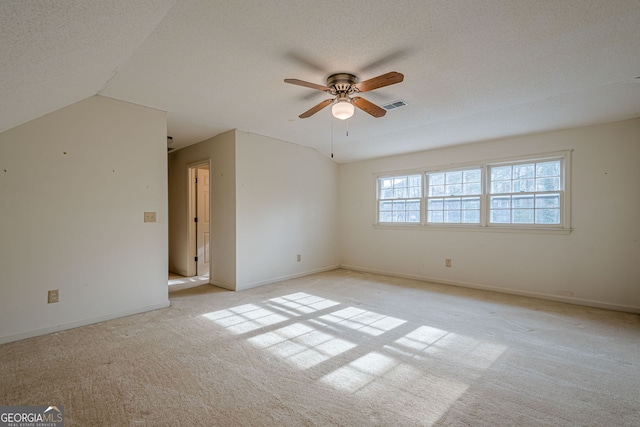 spare room with ceiling fan, vaulted ceiling, light carpet, and a textured ceiling