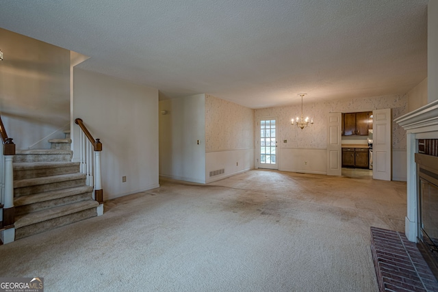 unfurnished living room with light colored carpet, a textured ceiling, a chandelier, and a fireplace