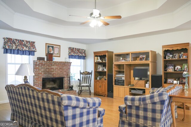 living room featuring a tray ceiling, a brick fireplace, and light wood-type flooring