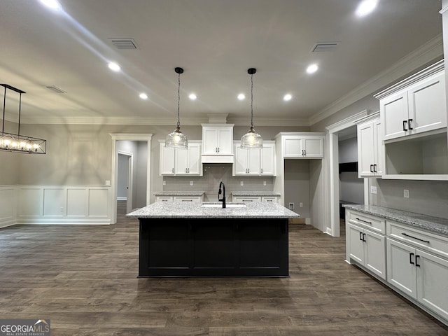 kitchen featuring light stone counters, white cabinets, a kitchen island with sink, and pendant lighting