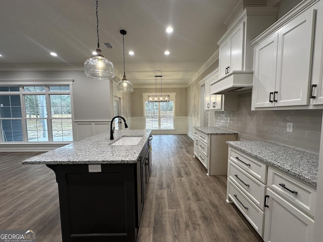 kitchen with sink, white cabinetry, hanging light fixtures, light stone counters, and a center island with sink