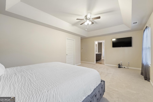 carpeted bedroom with ceiling fan, ensuite bathroom, and a tray ceiling