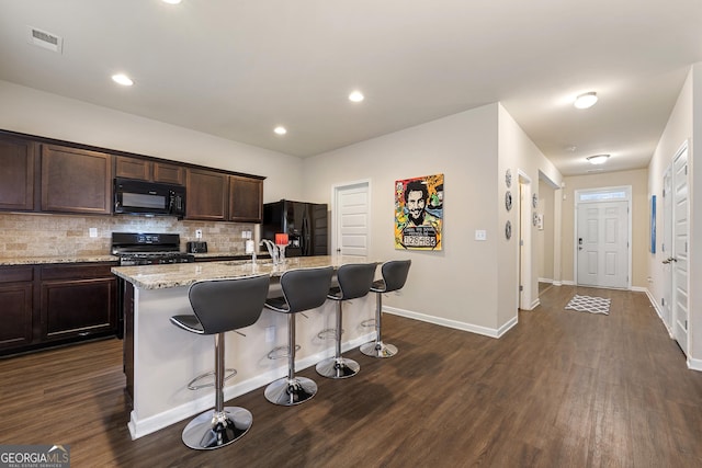 kitchen featuring a kitchen breakfast bar, light stone counters, tasteful backsplash, black appliances, and an island with sink