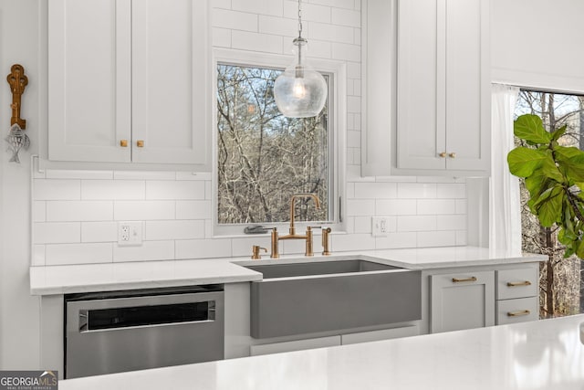 kitchen featuring sink, dishwasher, white cabinetry, hanging light fixtures, and decorative backsplash