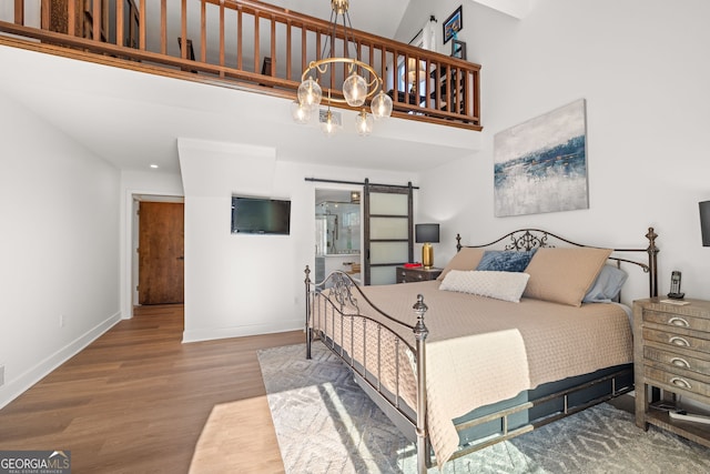 bedroom with a notable chandelier, hardwood / wood-style flooring, a barn door, and a towering ceiling