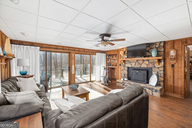 living room with a drop ceiling, hardwood / wood-style floors, a stone fireplace, and wood walls