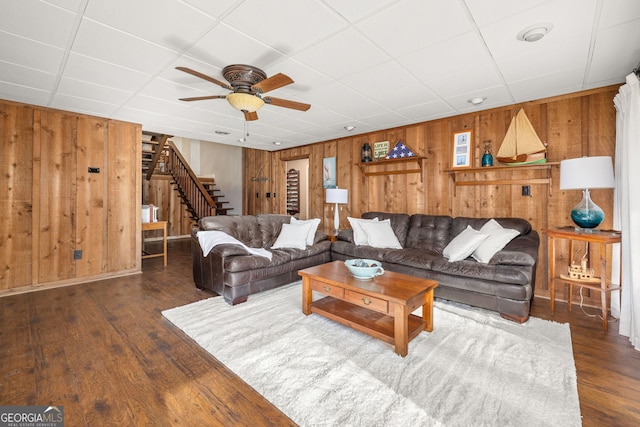 living room featuring dark wood-type flooring, ceiling fan, and wooden walls