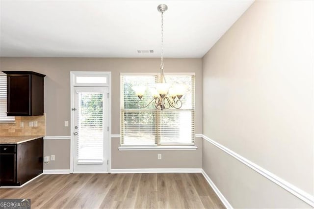 unfurnished dining area featuring plenty of natural light, a chandelier, and light hardwood / wood-style flooring