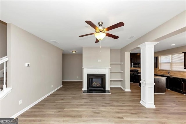 unfurnished living room with ceiling fan, sink, light hardwood / wood-style flooring, and ornate columns