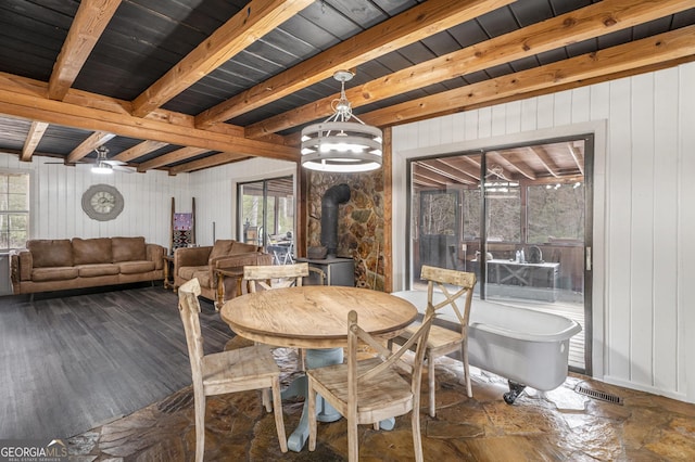 dining room with beamed ceiling, a wood stove, and a wealth of natural light