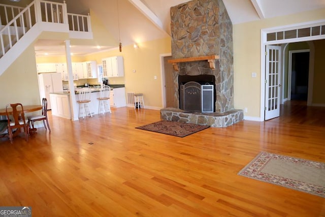 unfurnished living room featuring high vaulted ceiling, a fireplace, light wood-type flooring, beam ceiling, and french doors