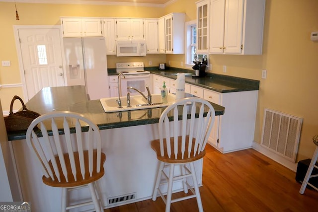 kitchen featuring a kitchen breakfast bar, white cabinetry, hardwood / wood-style flooring, and white appliances