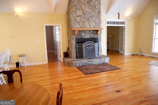 unfurnished living room featuring lofted ceiling with beams, wood-type flooring, and a stone fireplace