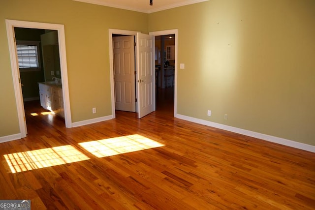 unfurnished bedroom featuring ornamental molding, a walk in closet, ensuite bath, and light hardwood / wood-style flooring