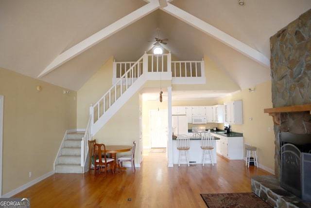 living room with a stone fireplace, high vaulted ceiling, beamed ceiling, ceiling fan, and light hardwood / wood-style floors