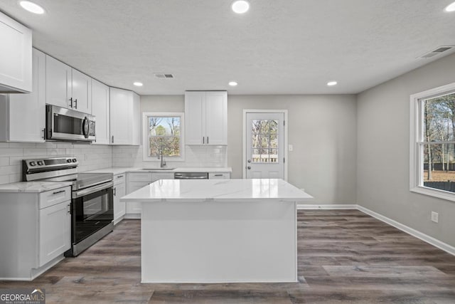 kitchen with sink, appliances with stainless steel finishes, a center island, light stone countertops, and white cabinets