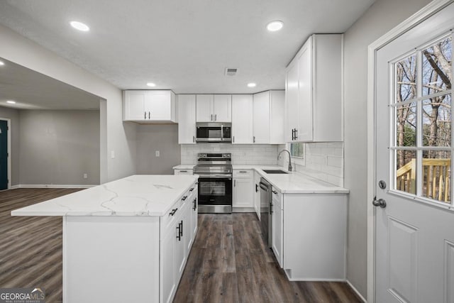 kitchen featuring appliances with stainless steel finishes, white cabinetry, sink, a center island, and light stone counters