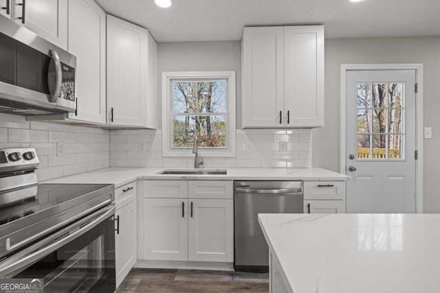 kitchen featuring white cabinetry, sink, backsplash, stainless steel appliances, and light stone countertops