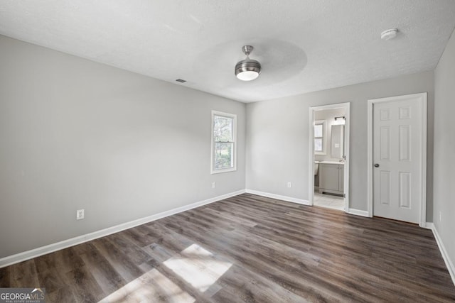 unfurnished bedroom featuring ceiling fan, connected bathroom, a textured ceiling, and dark hardwood / wood-style flooring