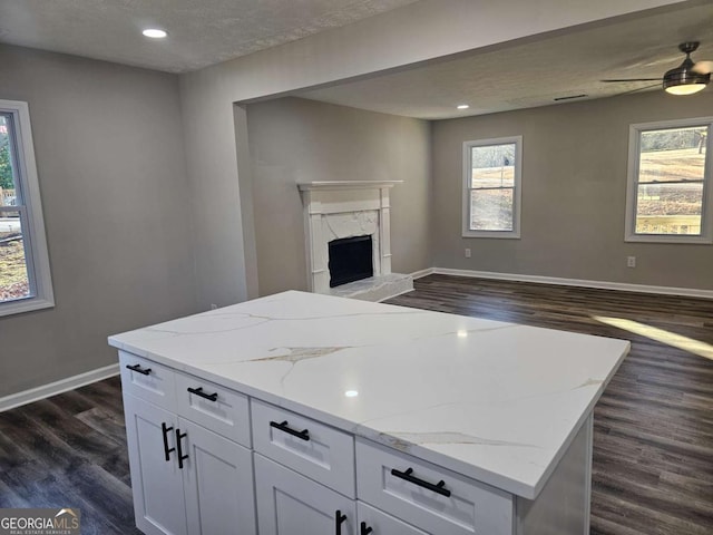 kitchen with light stone counters, a high end fireplace, dark hardwood / wood-style flooring, and white cabinets