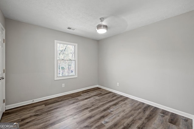 empty room with dark hardwood / wood-style floors and a textured ceiling