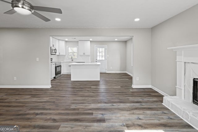 unfurnished living room with sink, dark wood-type flooring, a premium fireplace, and ceiling fan