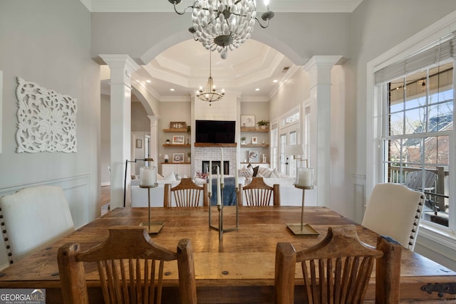 dining space featuring a raised ceiling, ornamental molding, an inviting chandelier, and ornate columns