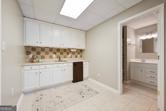 interior space featuring white cabinetry, sink, a drop ceiling, and backsplash