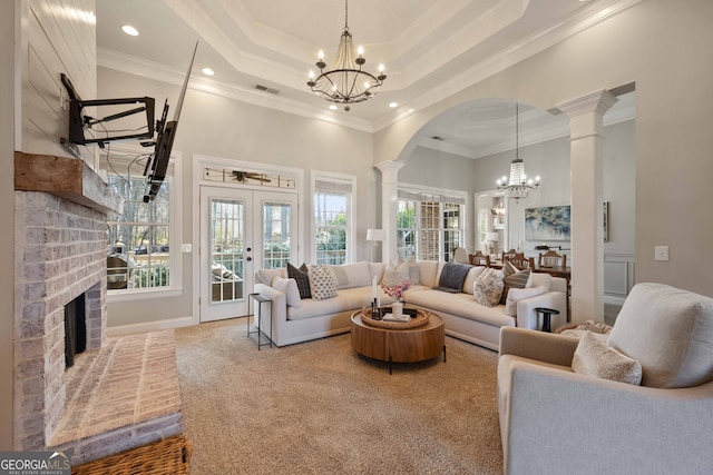 living room featuring an inviting chandelier, decorative columns, a raised ceiling, and french doors