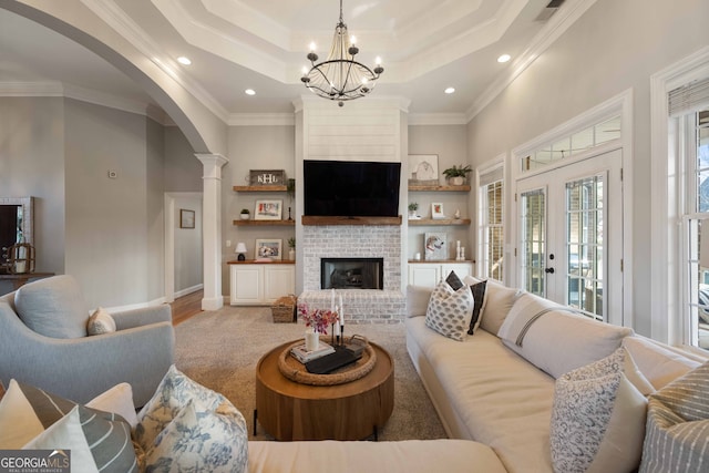 living room with french doors, crown molding, a brick fireplace, a raised ceiling, and a notable chandelier