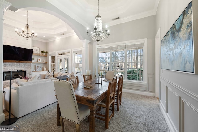 dining room featuring a fireplace, carpet floors, ornamental molding, a raised ceiling, and an inviting chandelier