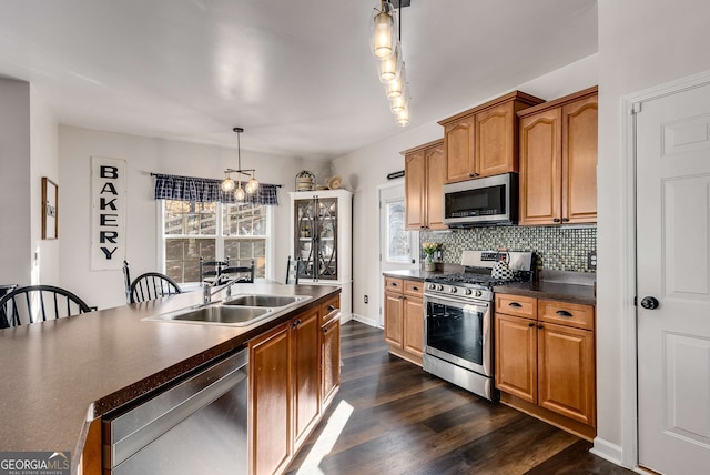 kitchen featuring appliances with stainless steel finishes, decorative light fixtures, sink, backsplash, and dark wood-type flooring