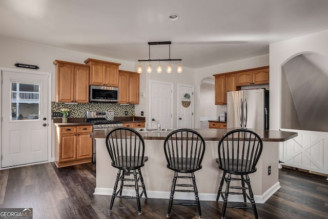 kitchen featuring pendant lighting, stainless steel appliances, dark hardwood / wood-style flooring, and an island with sink