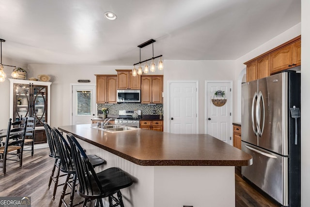 kitchen featuring tasteful backsplash, dark hardwood / wood-style floors, pendant lighting, stainless steel appliances, and a kitchen island with sink