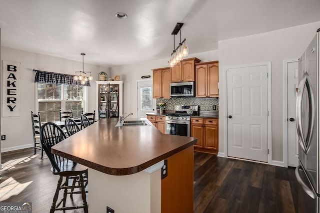 kitchen featuring appliances with stainless steel finishes, an island with sink, sink, a kitchen breakfast bar, and hanging light fixtures