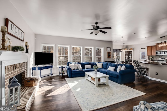 living room with dark wood-type flooring, ceiling fan, and a brick fireplace