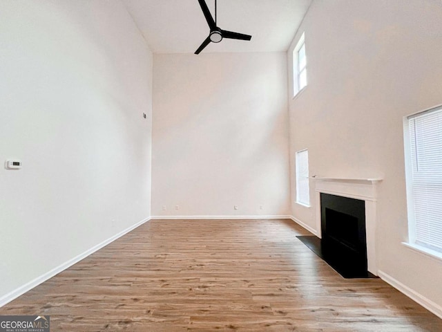 unfurnished living room featuring a high ceiling, ceiling fan, and light wood-type flooring