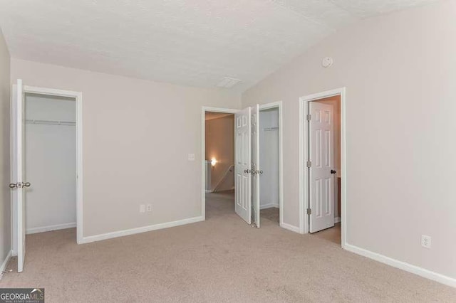 unfurnished bedroom featuring vaulted ceiling, light colored carpet, and a textured ceiling