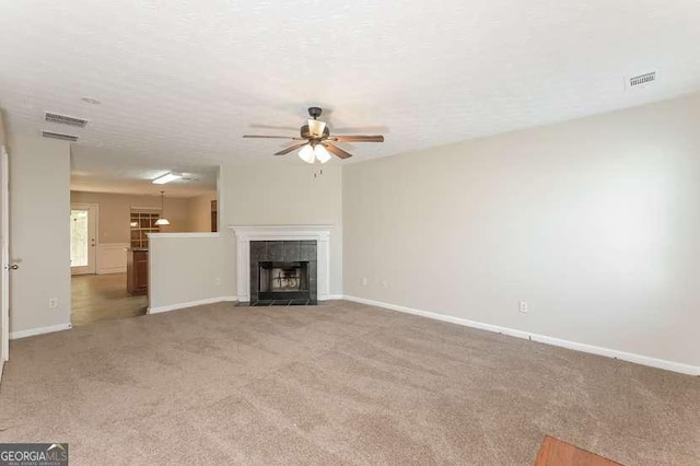 unfurnished living room featuring ceiling fan, light colored carpet, a tiled fireplace, and a textured ceiling