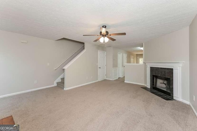 unfurnished living room with ceiling fan, a tiled fireplace, carpet, and a textured ceiling