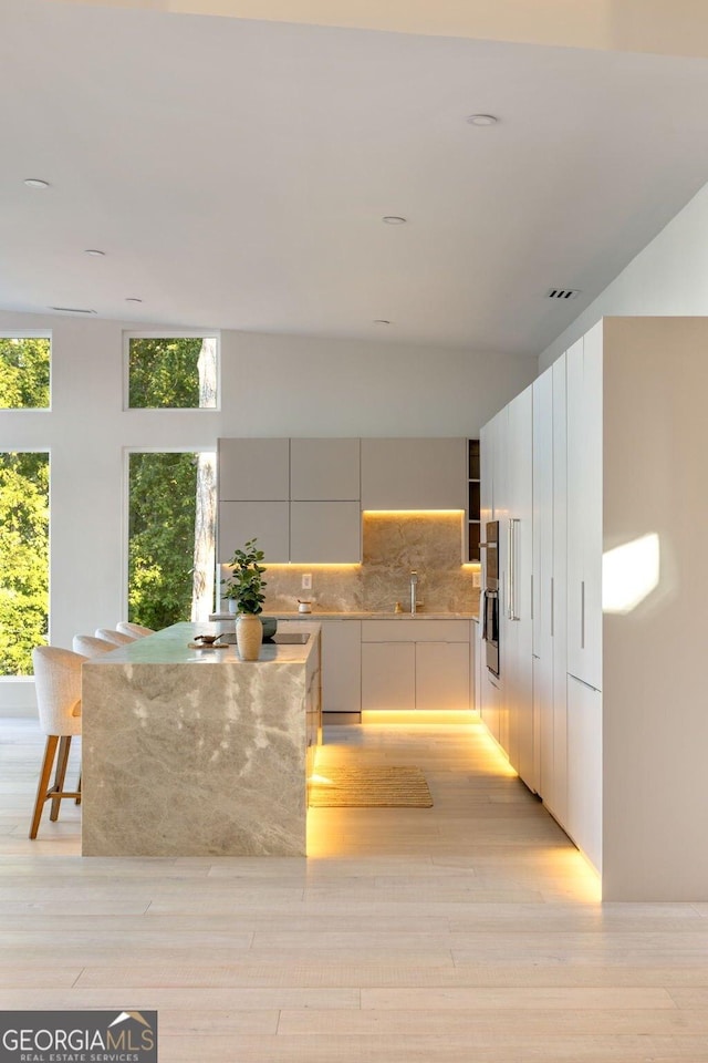 kitchen with backsplash, a breakfast bar area, a healthy amount of sunlight, and light wood-type flooring