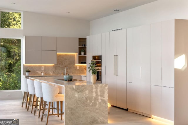 kitchen with a healthy amount of sunlight, backsplash, light hardwood / wood-style floors, and a breakfast bar