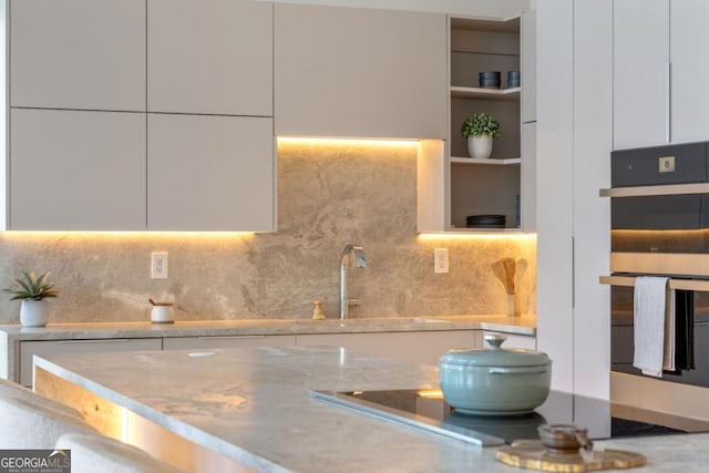 kitchen featuring tasteful backsplash, white cabinetry, sink, and double oven