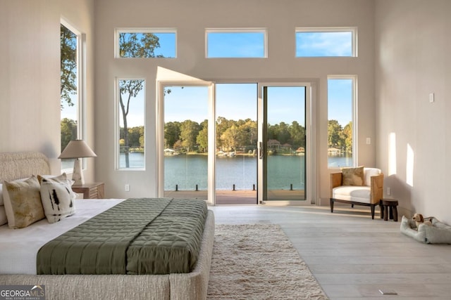 bedroom featuring access to exterior, hardwood / wood-style floors, and a water view