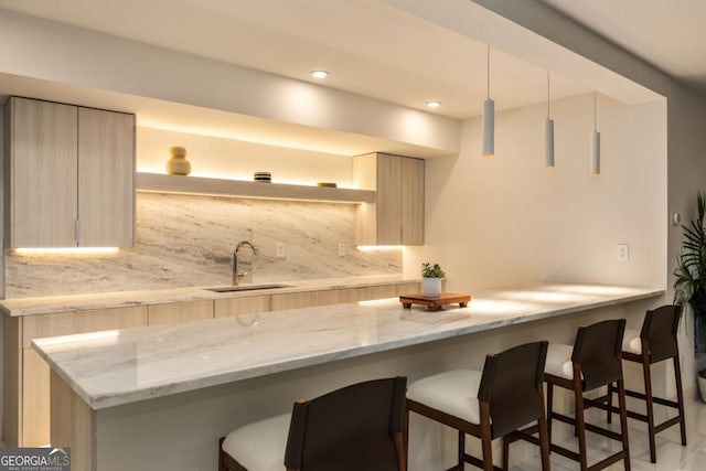 kitchen with light brown cabinetry, sink, backsplash, and light stone countertops