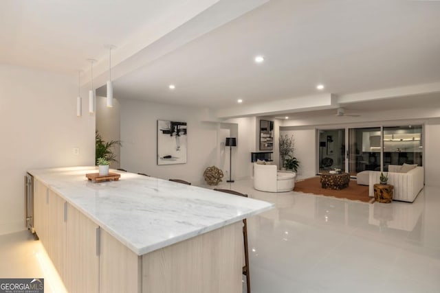 kitchen with light brown cabinetry, light stone counters, decorative light fixtures, and light tile patterned flooring